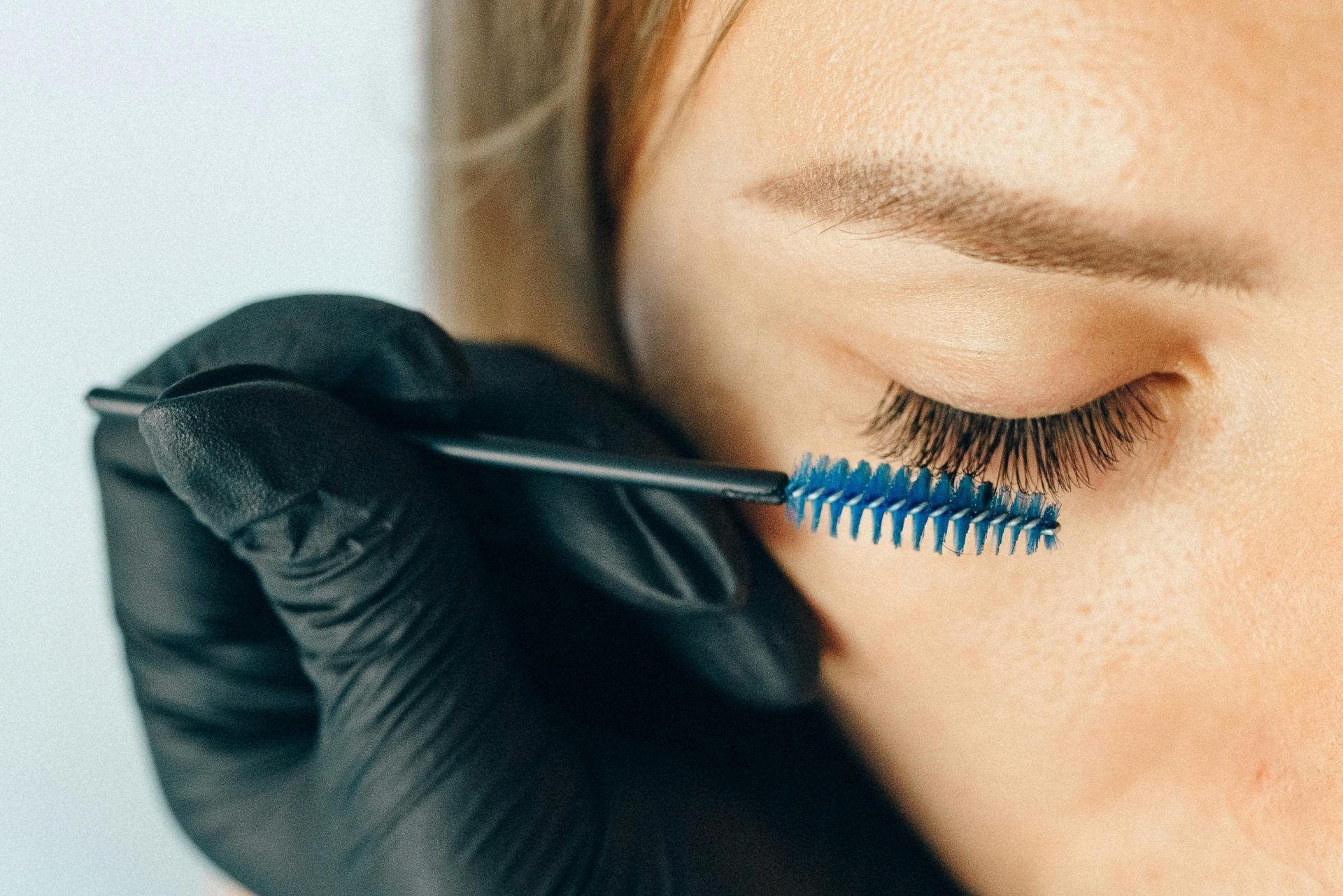 Una profesional aplica extensiones de pestañas utilizando un pincel aplicador azul para lograr un aspecto sofisticado.