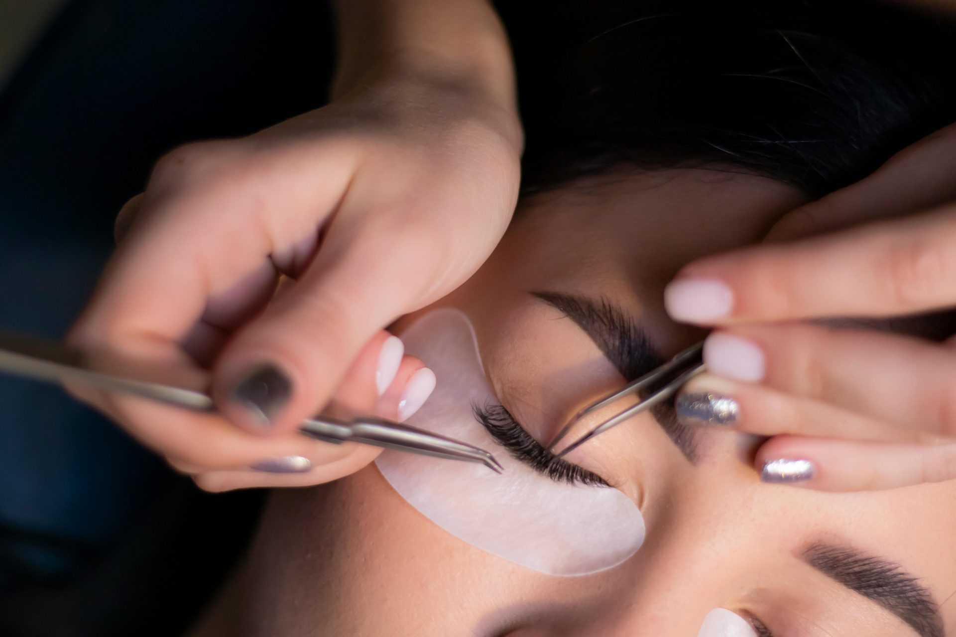 Vista detallada de una esteticista aplicando extensiones de pestañas en los ojos de una mujer.